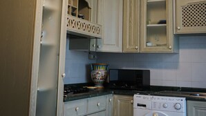 Een keuken met houten kastjes, een fornuis, een magnetron en een wasmachine.