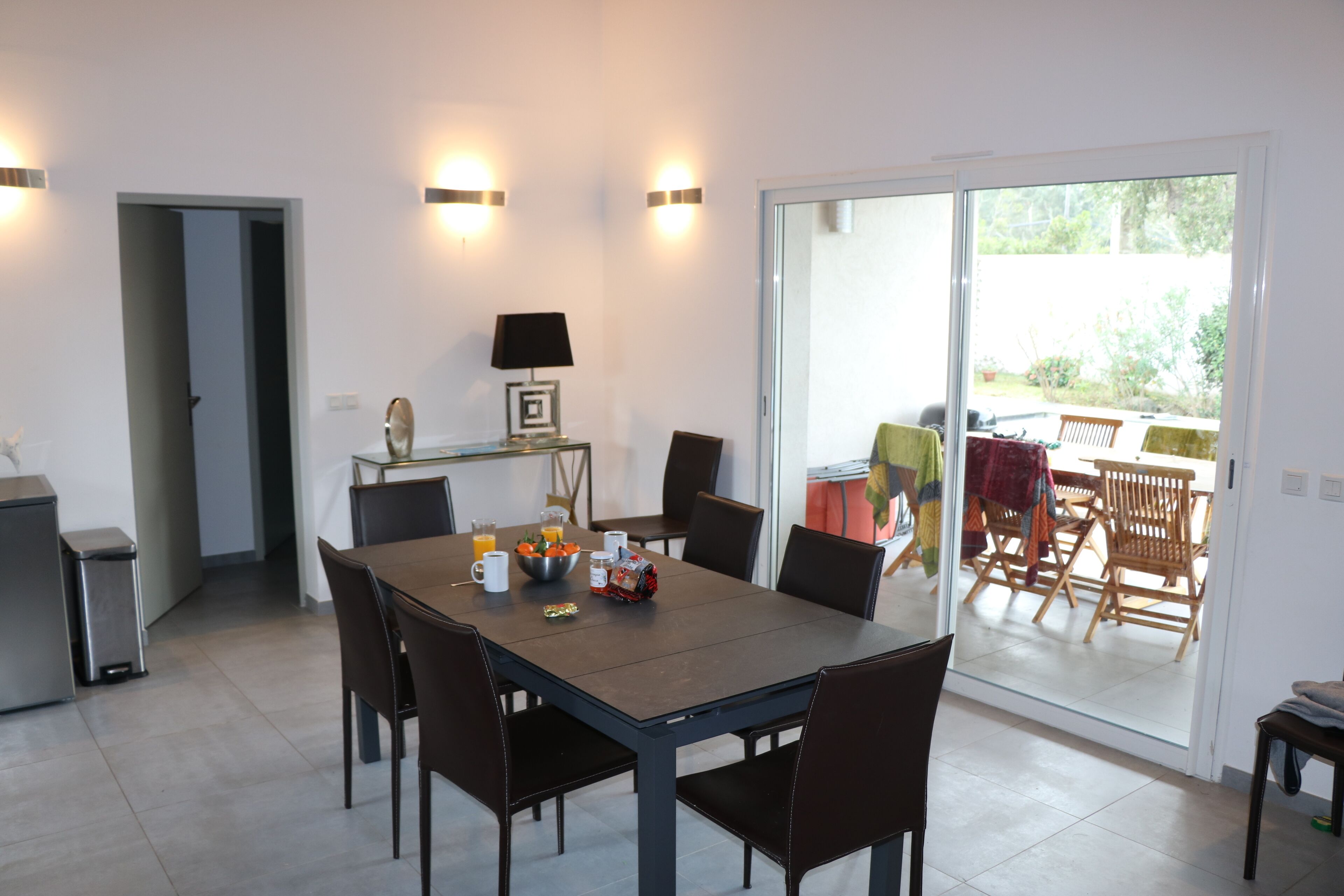 Un coin repas avec une table dressée pour quatre personnes, une lampe et un saladier de fruits posé sur la table.