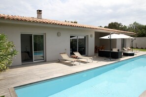 Ein modernes Haus mit Swimmingpool, Holzterrasse und Sitzbereich im Freien.