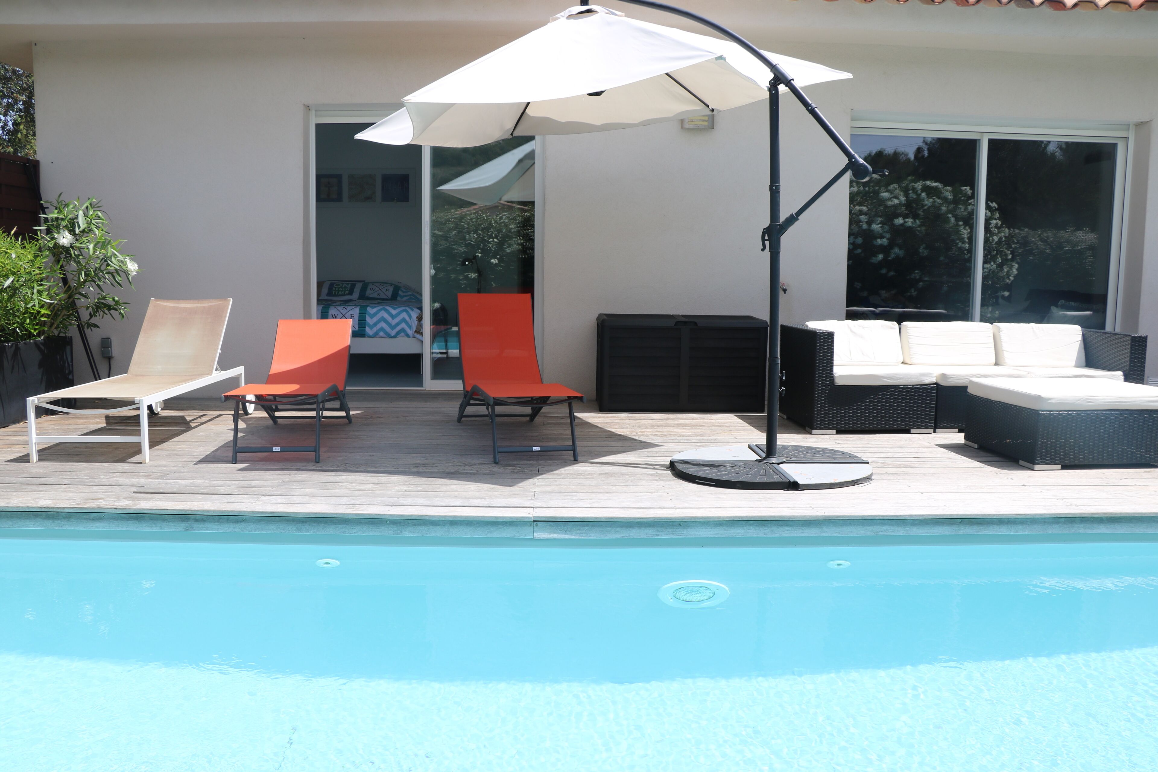 Un espace aménagé au bord de la piscine, comprenant une piscine, des chaises longues, une table et un grand parasol.