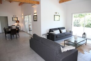 Ein modernes Wohnzimmer mit einem grauen Sofa, einem Glastisch und einem Essbereich mit Stühlen und Tisch.