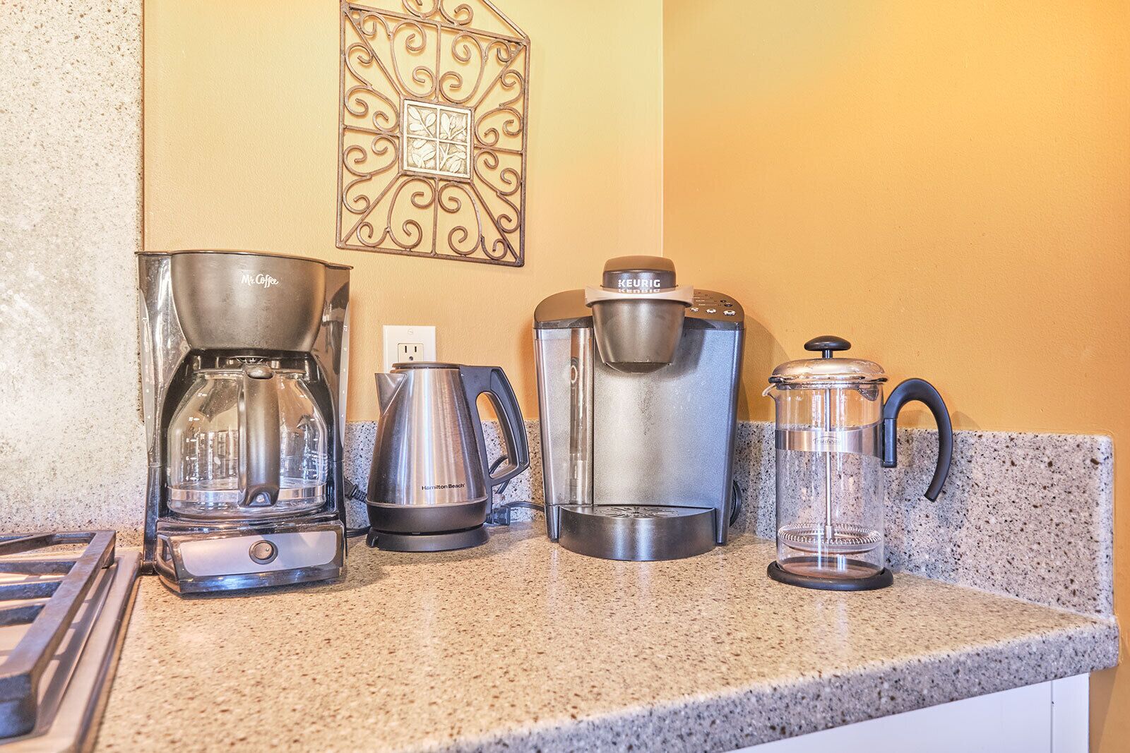 A kitchen counter with a coffee maker, a kettle, a French press, and a glass carafe.
