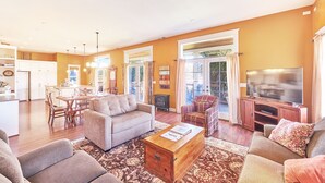 A spacious living room with a sofa, coffee table, and a television. There is a dining area with a table and chairs, and a kitchen in the background. - Dogs friendly, In Town, Walk to Everything (BeachyK) (Long Beach)