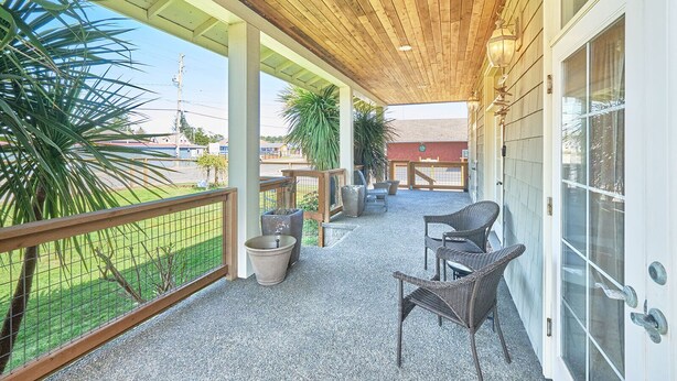 A covered outdoor area with a wooden ceiling, two wicker chairs, a concrete planter, and a view of a green field and buildings in the background. - Dogs friendly, In Town, Walk to Everything (BeachyK) (Long Beach)