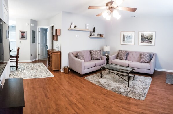Sala de estar con piso de madera, dos sofás, una mesa de centro y un ventilador de techo.