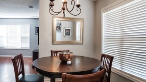A dining room with a round table, four wooden chairs, a chandelier, and a large window with blinds. - College Town Retreat! Close to UGA and Downtown! (Athens)