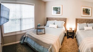 A bedroom with two beds, a bedside table with a lamp, and a window with blinds. - College Town Retreat! Close to UGA and Downtown! (Athens)