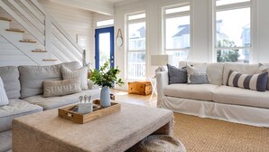 A living room with a staircase, a blue door, and a view of houses through large windows. - The Big Dream Getaway 💙Private Heated Pool Sleeps 13 (Atlantic Beach)