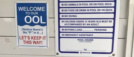 A wall with multiple signs including 'POOL RULES', 'WELCOME TO OUR OOL', and 'NO DIVING ALLOWED'.