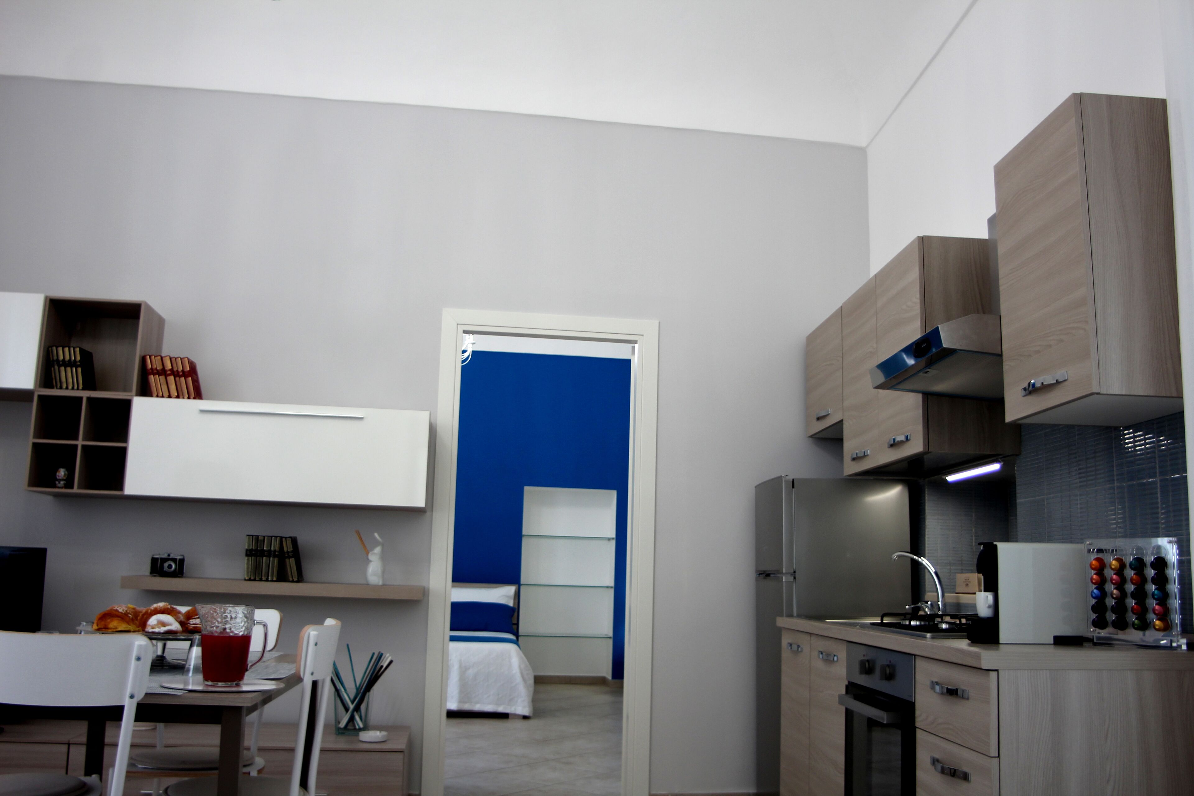 Una cucina moderna con elettrodomestici integrati, un'area pranzo con tavolo e sedie, e una camera da letto con una porta blu.