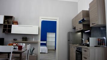 Una cucina moderna con elettrodomestici integrati, un'area pranzo con tavolo e sedie, e una camera da letto con una porta blu.