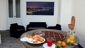 A breakfast setup with pastries, a drink, and fresh fruit on a stone table, with a cityscape view in the background. - GARDEN OF THE VESUVIUS (Terzigno)