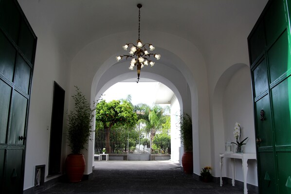 A corridor with a chandelier, potted plants, and a view of a garden through an archway. - GARDEN OF THE VESUVIUS (Terzigno)