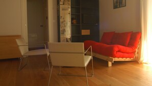 A room with a wooden floor, a white chair, a red sofa, and a black cabinet with papers. - An oasis of peace: the Honey House (PINEROLO)