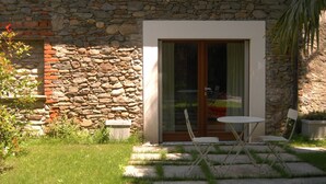 A stone house with a glass door and a small patio with two chairs and a table. - An oasis of peace: the Honey House (PINEROLO)