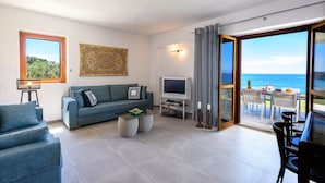 A living room with a sofa, TV, and a table with a view of the ocean.