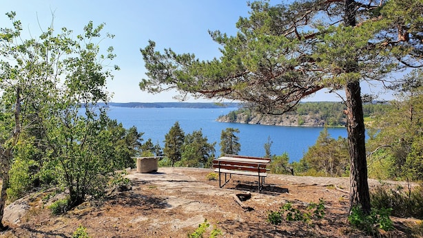 A bench and a stone structure in a natural setting with a view of a lake and distant land.