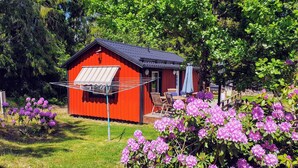 A red wooden cabin with a black roof, a clothesline, and a patio with chairs and a table.