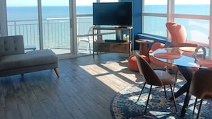 Uma sala de estar ampla, com uma TV grande, assentos confortáveis e vista para o oceano.