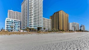 Um hotel à beira-mar com vários edifícios altos, uma praia de areia e céu claro.