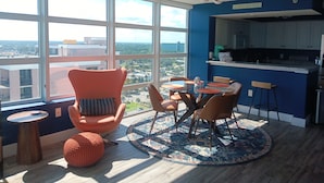 Cozinha moderna com parede azul de destaque, área de jantar com mesa e cadeiras redondas, e uma grande janela com vista para a cidade.