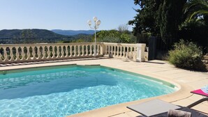 Une piscine à l’eau claire, entourée d’une balustrade beige. On y trouve des chaises longues avec des serviettes et un livre posé dessus.