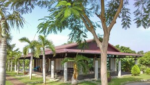A covered pavilion with a red roof, surrounded by palm trees and a grassy area. - Clove House (Hengchun)