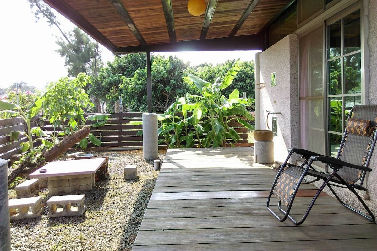 Un patio techado con terraza de madera, una silla de descanso y una maceta de piedra.