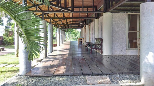 A covered outdoor area with wooden flooring, benches, and a palm tree. - Clove House (Hengchun)