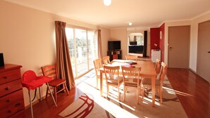 A bright living room with a dining area, a TV, and a balcony.