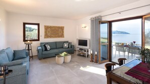 Un salon moderne avec un canapé, un téléviseur et un coin repas offrant une vue sur la mer.