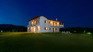 Une maison à deux étages dotée d’un balcon, d’un patio couvert et d’une pelouse avec des chaises longues.