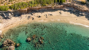 Vue aérienne d’une plage aux eaux turquoise et limpides, bordée de formations rocheuses et d’une végétation clairsemée.