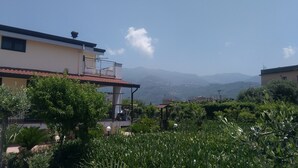 Ein Wohngebäude mit Balkon, umgeben von üppiger Vegetation und Bergen im Hintergrund.