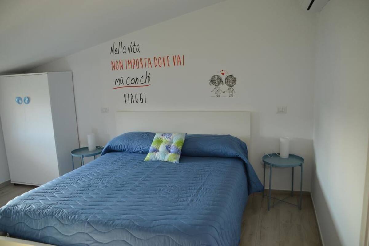 Une chambre à coucher avec un lit, deux tables de chevet, un mur orné d’une citation inspirante et un petit dessin représentant deux personnes.