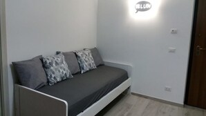Ein kleines, modernes Zimmer mit einem Einzelbett, einer Wandleuchte und einer Tür.