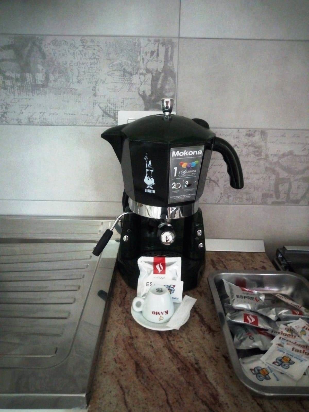 A coffee maker on a kitchen counter with a packet of coffee pods and a cup.