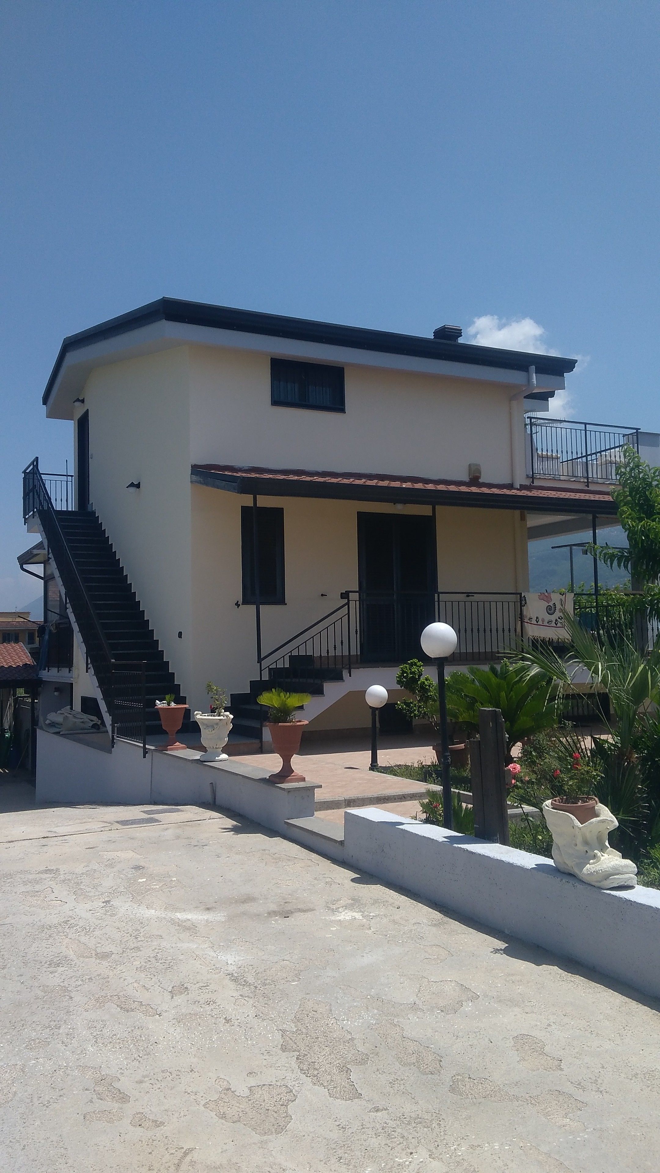 Ein zweigeschossiges Gebäude mit einer Treppe, die zum Eingang führt, einem Balkon mit Geländern und Topfpflanzen im Vordergrund.