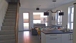A modern kitchen with a central island, a dining area with a sofa, and a staircase leading to an upper floor. - Reusenhaus South in Breege (Breege)
