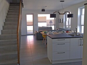 A modern kitchen with a central island, a dining area with a sofa, and a staircase leading to an upper floor. - Reusenhaus South in Breege (Breege)