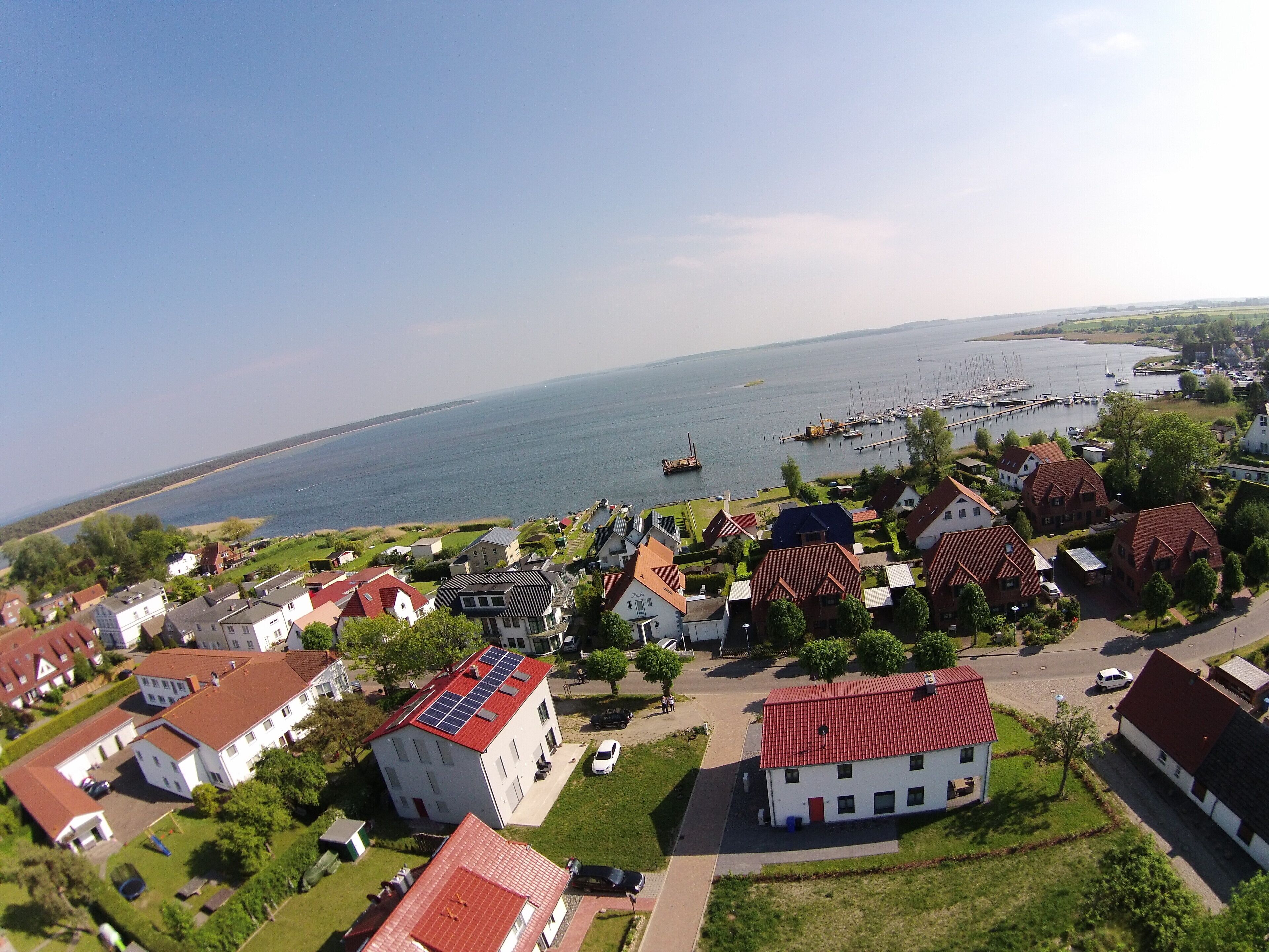 Ett bostadsområde vid kusten med hus, en småbåtshamn och utsikt över havet.