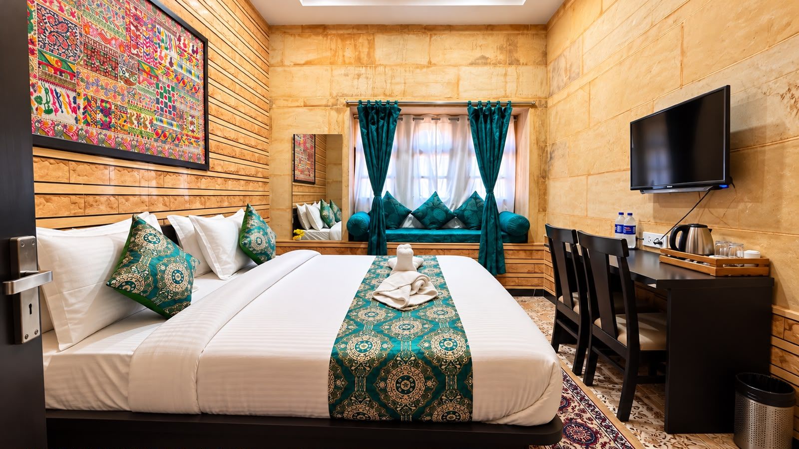 Una habitación de hotel con cama, escritorio, televisor y ventana con cortinas.