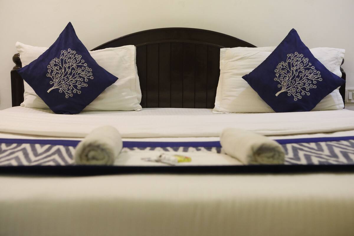 A bed with a dark headboard, two pillows with a tree design, and a patterned bedspread.