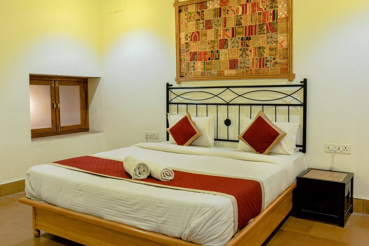 A neatly made bed with a red and white bedspread, a quilt, and two rolled towels.