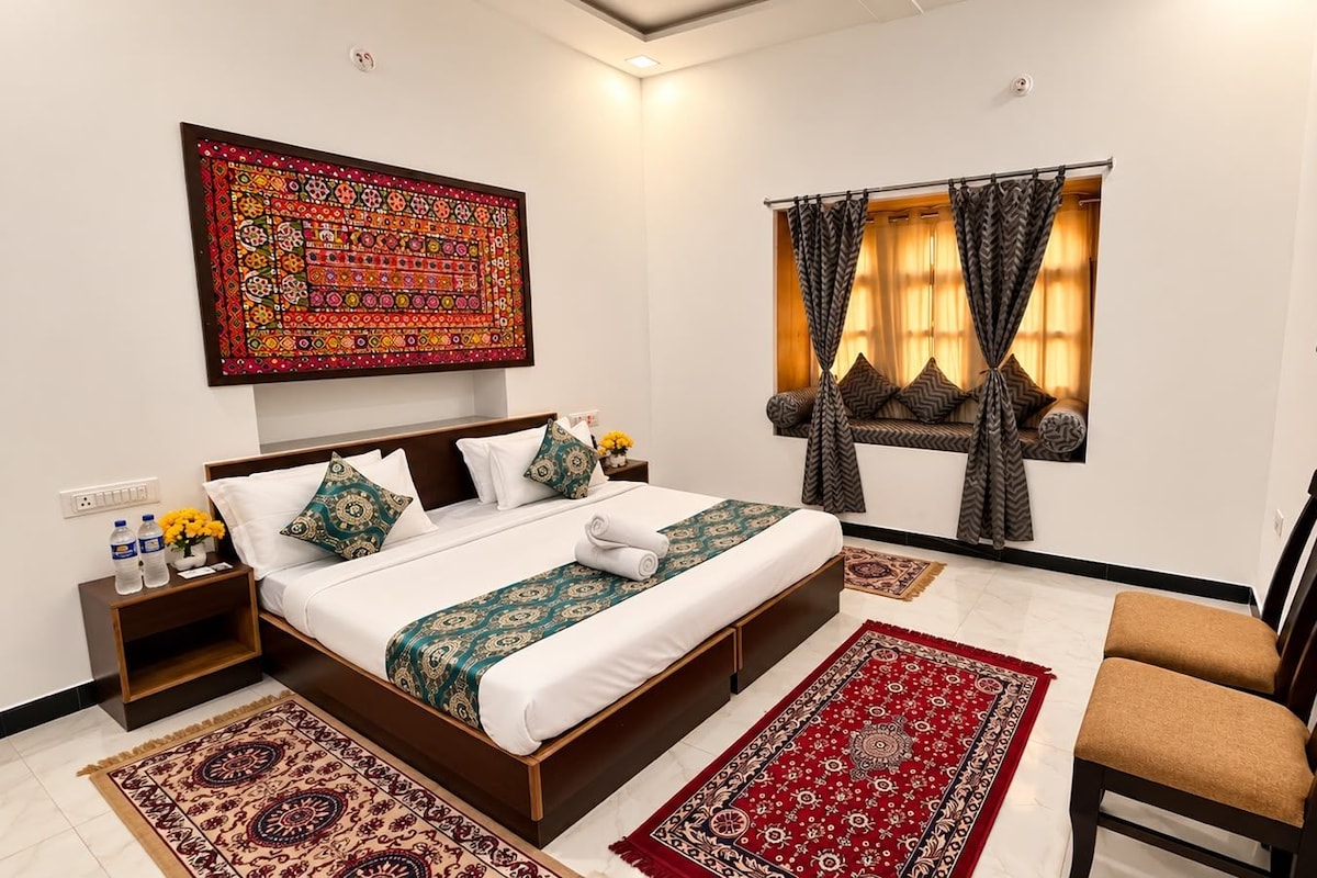 A hotel room with a bed, a chair, a TV, a window with curtains, a wall-mounted artwork, and a nightstand with a vase of flowers.