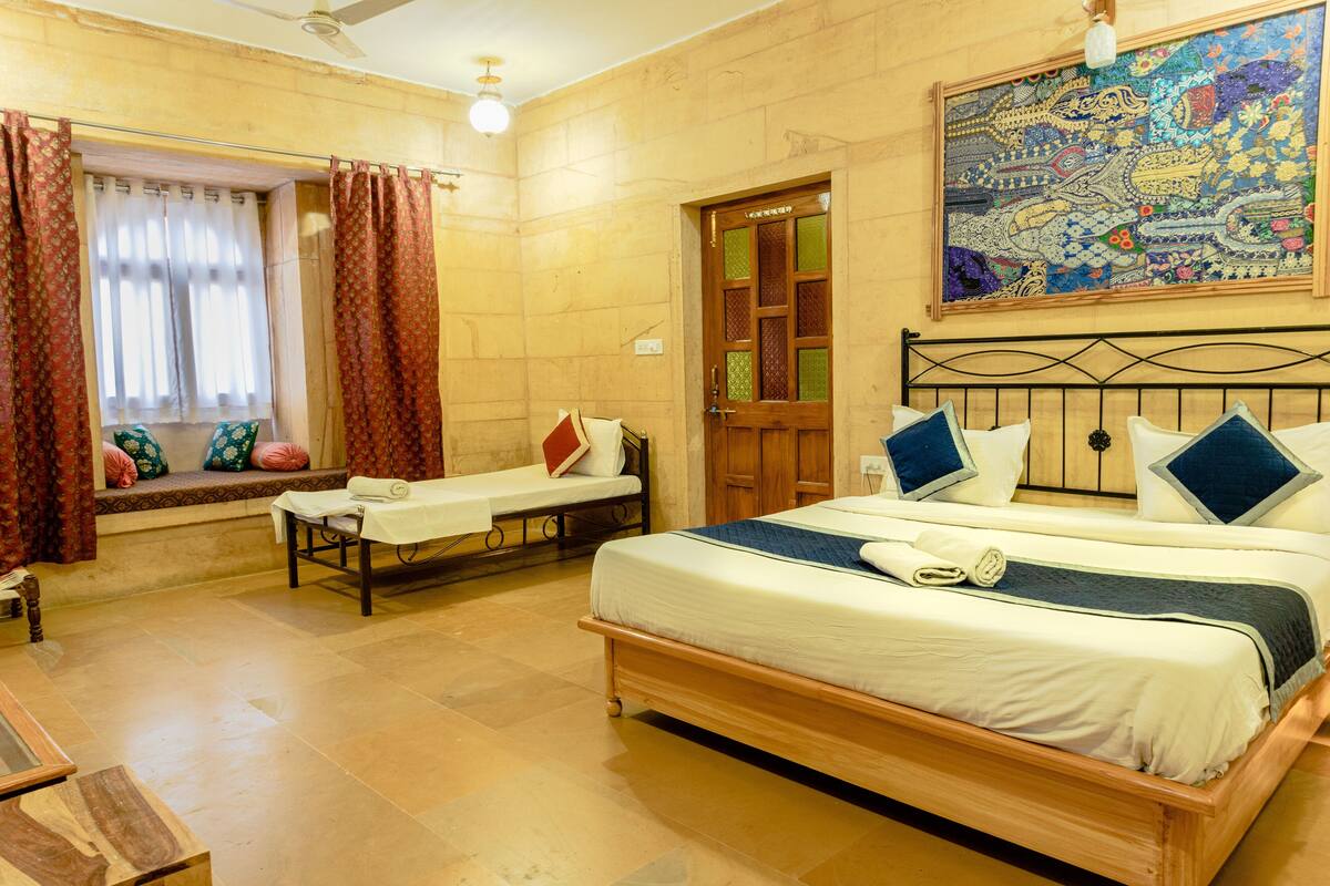 A hotel room with a bed, a bench, a window with curtains, a door, and a wall painting.