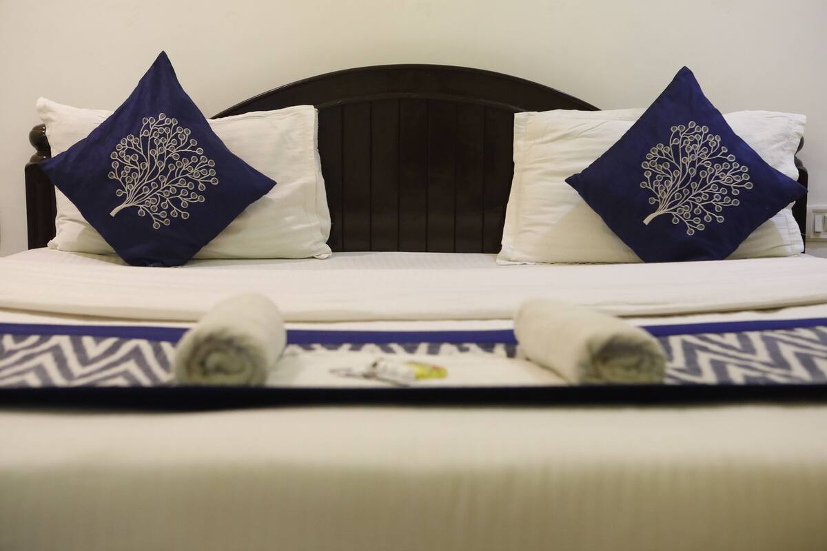 A bed with a dark headboard, two pillows with a tree design, and a patterned bedspread.