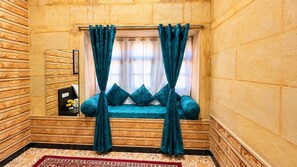 A room with a built-in bench, teal curtains, and a patterned rug. - Hotel Swan Haveli (Jaisalmer)