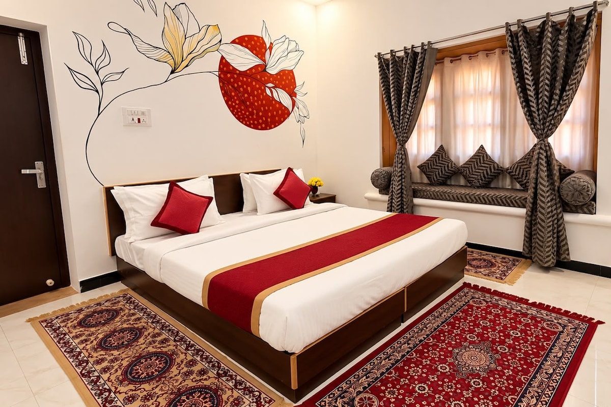 A hotel room with a large bed, a window with curtains, a wall mural, and a patterned rug.