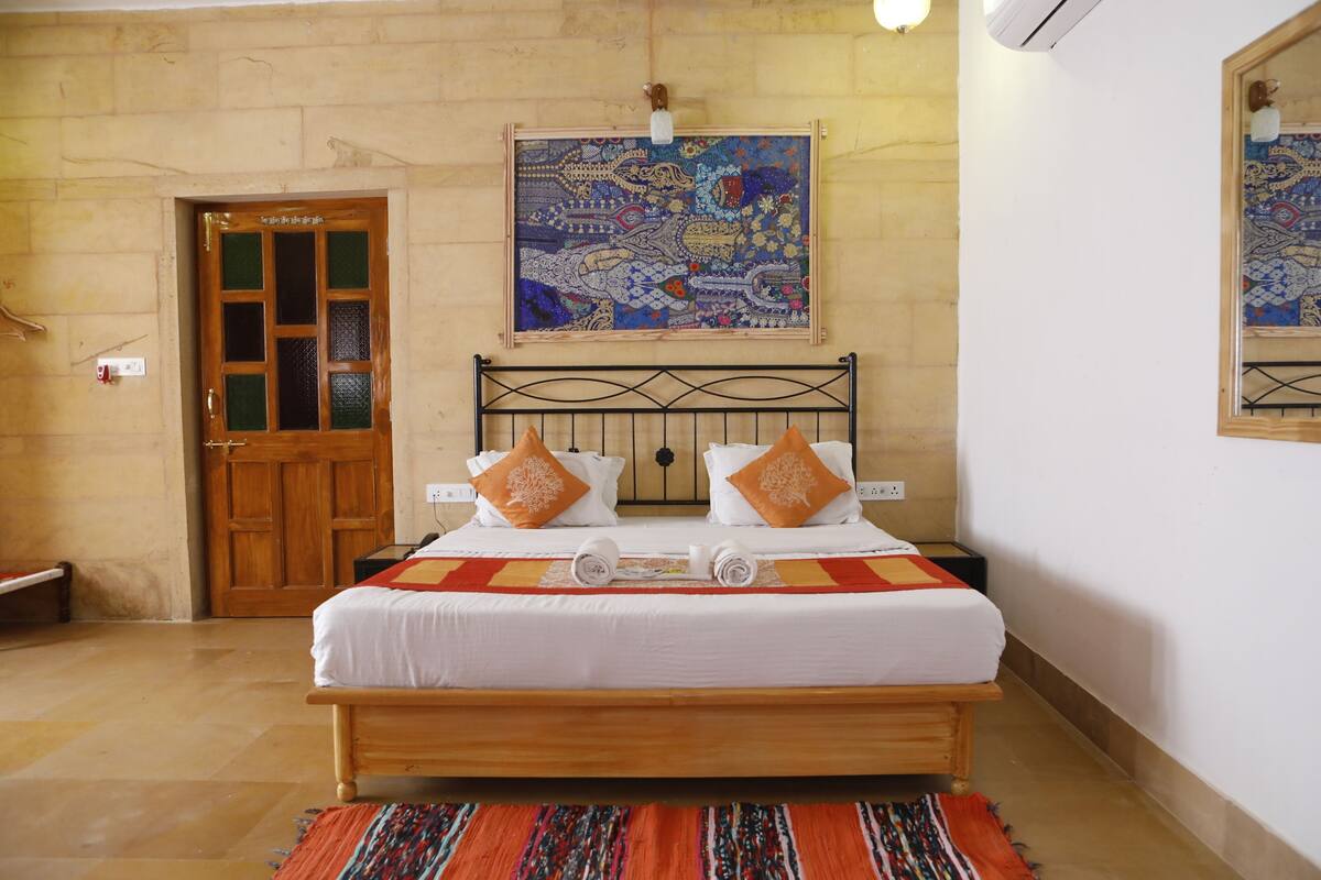 A bedroom with a wooden bed, two pillows, a colorful rug, a door, and a wall with a patterned artwork.